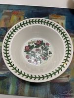 Top view of a white ceramic bowl showing green leafy rim with floral design in the center and small dragonfly motif