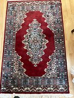 Full view of the red wool rug showing central medallion and border design with geometric/floral patterns