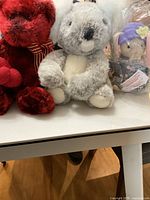 Red plush bear and gray plush koala sitting side by side on a white surface.