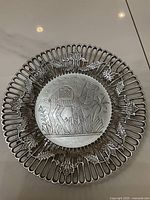 Front view of the silver openwork metal decor plate displaying an embossed camel design in the center with palm trees and floral patterns around the edge.