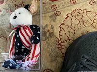 Photo of Ty Beanie Baby bear in clear display case showing the American flag fabric design and tag on ear.