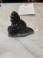 Side view of the small black soapstone Inuit carving on a reflective surface