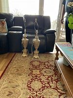 Photo showing two vintage table lamps placed side by side on a patterned rug in a living room setting in front of a loveseat.