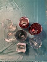 Top-down view showing all nine vases arranged on a teal cloth, including 2 red tall, 2 teal tall, and 5 clear vases of varying shapes and sizes.