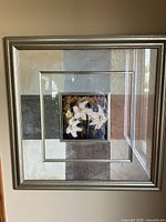 Full frontal view of the framed artwork showing the white lilies central print and the silver-tone frame with matte colors around the center.