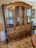 Front view of the solid wood china cabinet showing glass doors, shelves, drawers, and carved top detail.