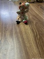 Photo of a ceramic sitting clown figurine on a wooden surface showing the clown holding a white ball with green design and wearing a small black hat.