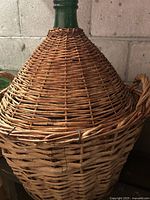 Close-up of the middle and upper half of the demijohn showing the tight basket weave covering the green glass and side handles