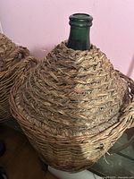 Close-up side view of green demijohn glass bottle with woven basket weave covering and side handles.