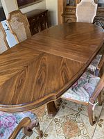 Oval wooden dining table with detailed wood grain finish and two extension leaves placed at the center.