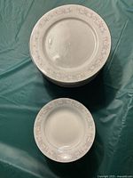 Top view of stacked dinner plates and a bowl placed on a teal fabric surface.