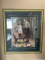 Framed print showing detailed scene of old man and girl, framed in gold-toned wood with decorative edges.