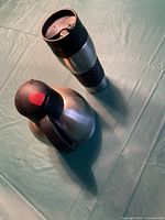 Photo of a stainless steel insulated decanter with black handle and push-button lid, next to a stainless steel travel mug with black grip and lid.