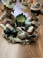 Front view of the Italian porcelain figurine featuring a boy and girl, two white swans, and a green leaf centerpiece on a decorative base.