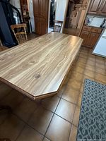 Top view of long rectangular solid wood kitchen table with polished veneer surface showing natural wood grain pattern and beveled ends.
