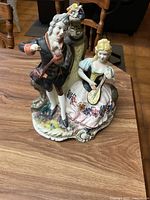 Front view of the porcelain figurine showing man standing with one arm raised beside a seated woman playing a mandolin, sitting on a multicolored base.