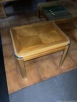 Mini end table with patterned wooden base and metal accents on rounded legs on tiled floor.