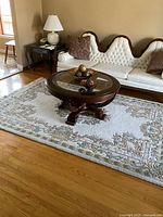 Living room setting showing the full 8 x 6 feet rug with floral and scroll design in pastel tones under a round glass coffee table and near a white tufted sofa.