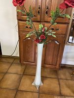 Full view of tall frosted glass vase with artificial red roses placed on floor in front of wooden cabinet.