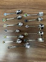 Full set of 12 small decorative spoons with city crests on handles laid out on wood surface.