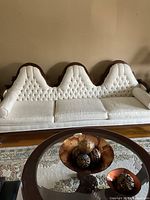 Front view of vintage sofa showing triple-arched tufted cream back cushions and seat cushions with dark wood frame.