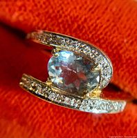Close-up of ring showing oval aquamarine centre and diamond accents against orange background