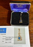 Pendant in black velvet box with blue satin lining lid and appraisal certificate beneath it showing photo and details of the pendant.