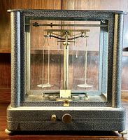 Front view of balance scale inside rectangular glass case with speckled metal frame showing brass beam and pans