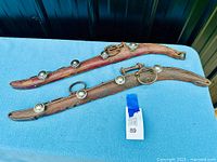 Two old, heavy wooden horse hames with attached metal coat hooks displayed on a blue fabric surface