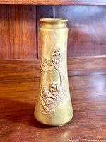 Full view of the tall brass vase against a wood background showing its shape and embossed design.