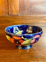 Front view of Moorcroft bowl showing the colorful pansy design around the exterior against a dark blue background.