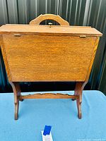 Front view of the antique oak sewing basket standing on blue cloth with visible handle and legs, closed flip-top lid