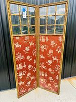 Full view of the antique folding screen showing two connected panels with ornate gold-painted wooden frames, glass panes at the top, and reddish patterned upholstered fabric at the bottom.