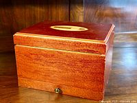 Full view of the wooden cigar humidor box closed, showing reddish-brown wood and an oval inlay on the lid.