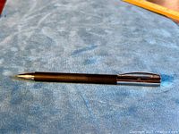 Full length image of black barrel pen with silver cap and tip, placed on blue textured surface.
