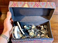 View of box filled with assorted jewellery including bangles, rings, earrings, and necklaces with a decorative outer box.