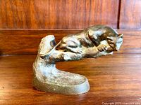 Side view of the bronze big cat sculpture placed on a wooden surface against a wood-paneled background.