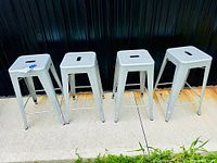 Four grey powder-coated pressed steel stools lined up side-by-side, showing overall height and design.