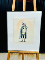 Framed original Batman drawing on easel showing full artwork and simple silver frame