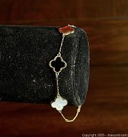 Gold wash sterling silver bracelet with clover-shaped stones in carnelian, onyx, and mother of pearl shown on black display stand.