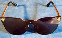 Full front view of Versace Medusa sunglasses showing black lenses with gold Medusa emblems on upper corners and brown temple arms.