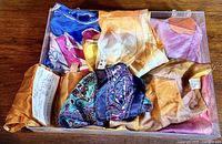 Overview of multiple silk scarves in vibrant colors and mixed patterns arranged together in a box.
