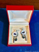 Pair of earrings in red jewelry box, showing front view, abalone bear motif on white circular background, hanging from silver-tone posts.