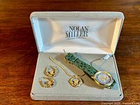 View of set in box showing gold-tone Claddagh pendant necklace, matching earrings, and quartz watch with green leather strap.