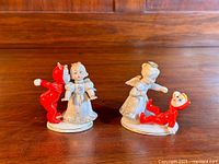 Front view of both figurines side by side on wooden surface showing angel and devil in fighting poses.