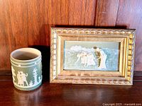 Front view of jasperware pot and framed embossed picture together, showing decorative classical figures on both items.
