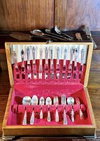 Full view of silverplated flatware set in wooden case with utensils and some loose serving flatware behind case