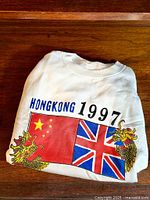 Folded white pullover sweater showing front graphic with Chinese and British flags and 'HONGKONG 1997' text.