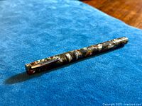 Fountain pen lying on blue fabric, showing full length and marbled pattern of body and cap.