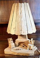 Front view of the vintage wooden table lamp showing a couple seated by a carved stone fireplace with campfire, and wooden slatted lampshade.